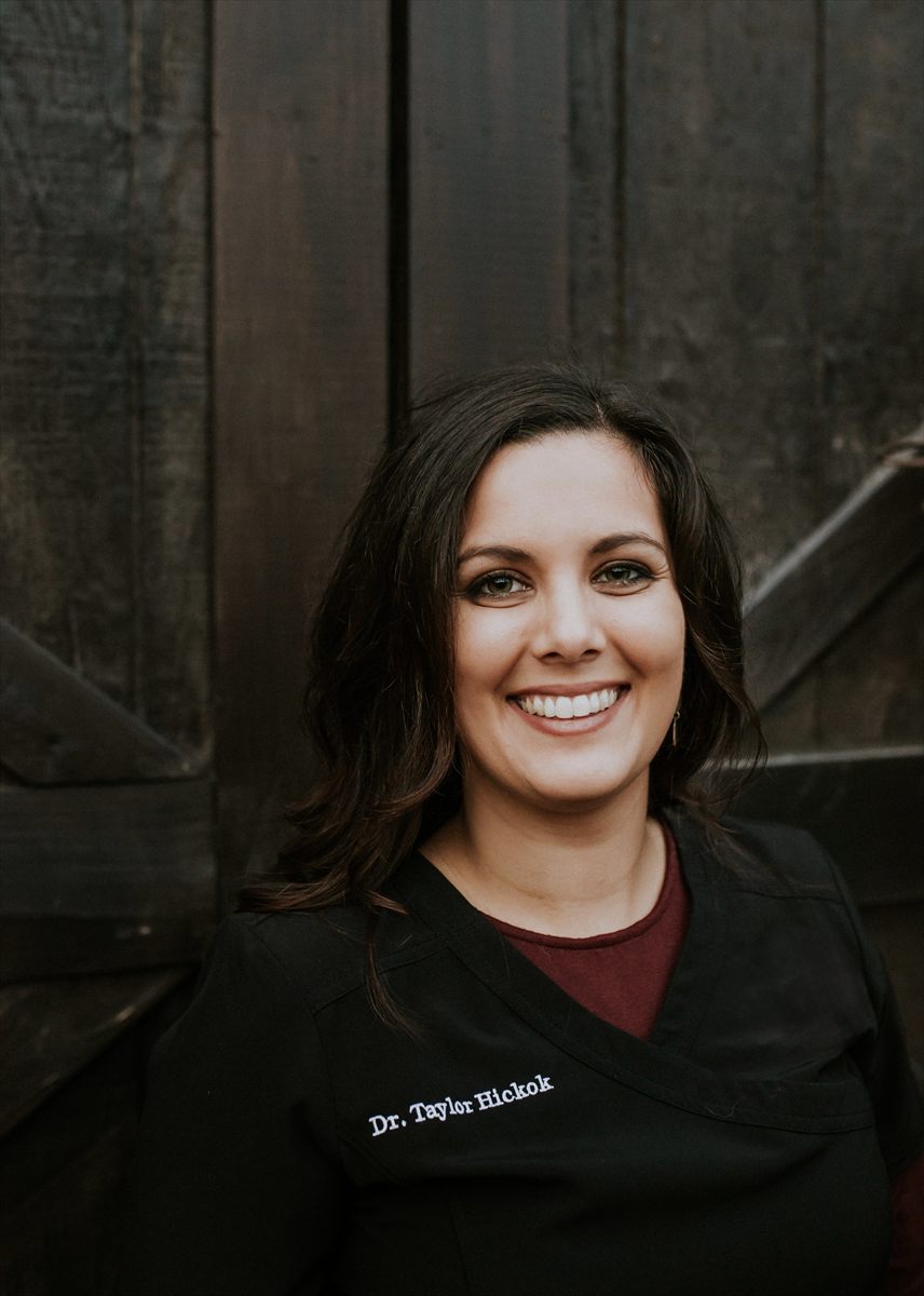 Portrait of Dr. Taylor Hickok, smiling, wearing black scrubs embroidered with her name.